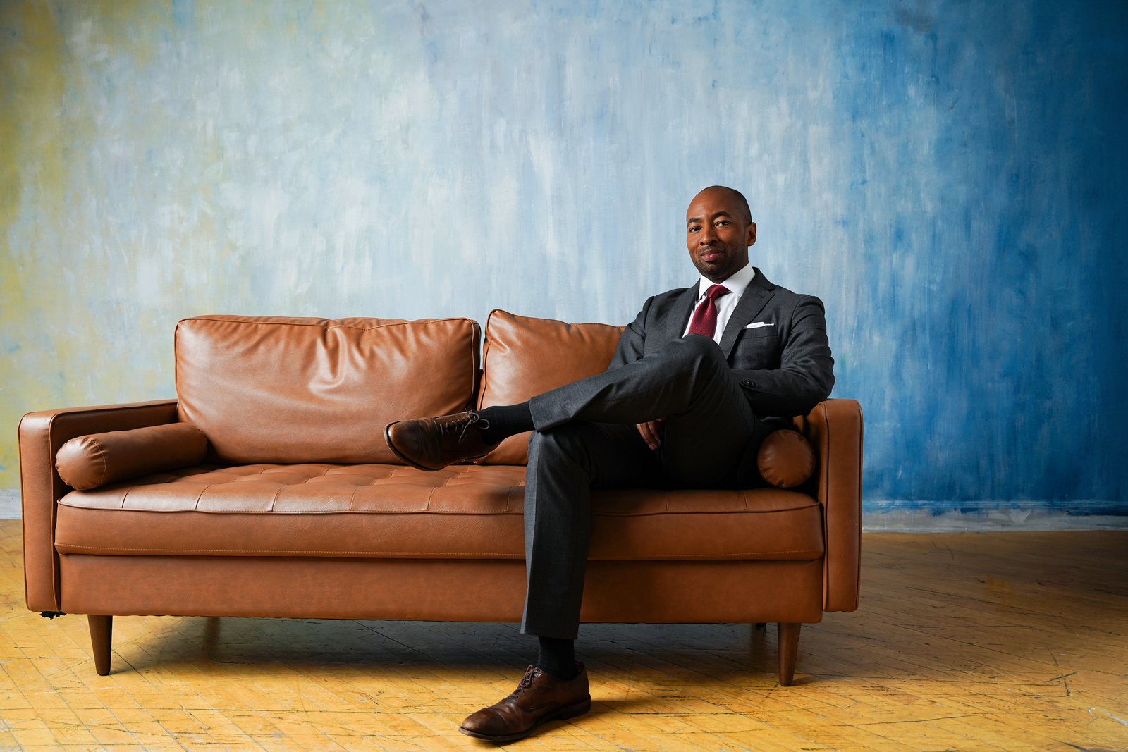 Wide frame, seated on a leather sofa against the blue backdrop