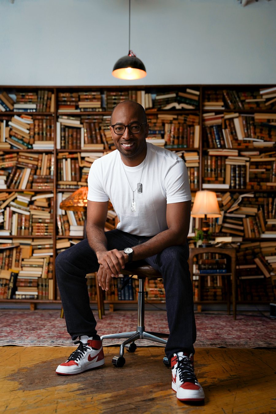 Portrait in a tee shirt seated before a wall of books