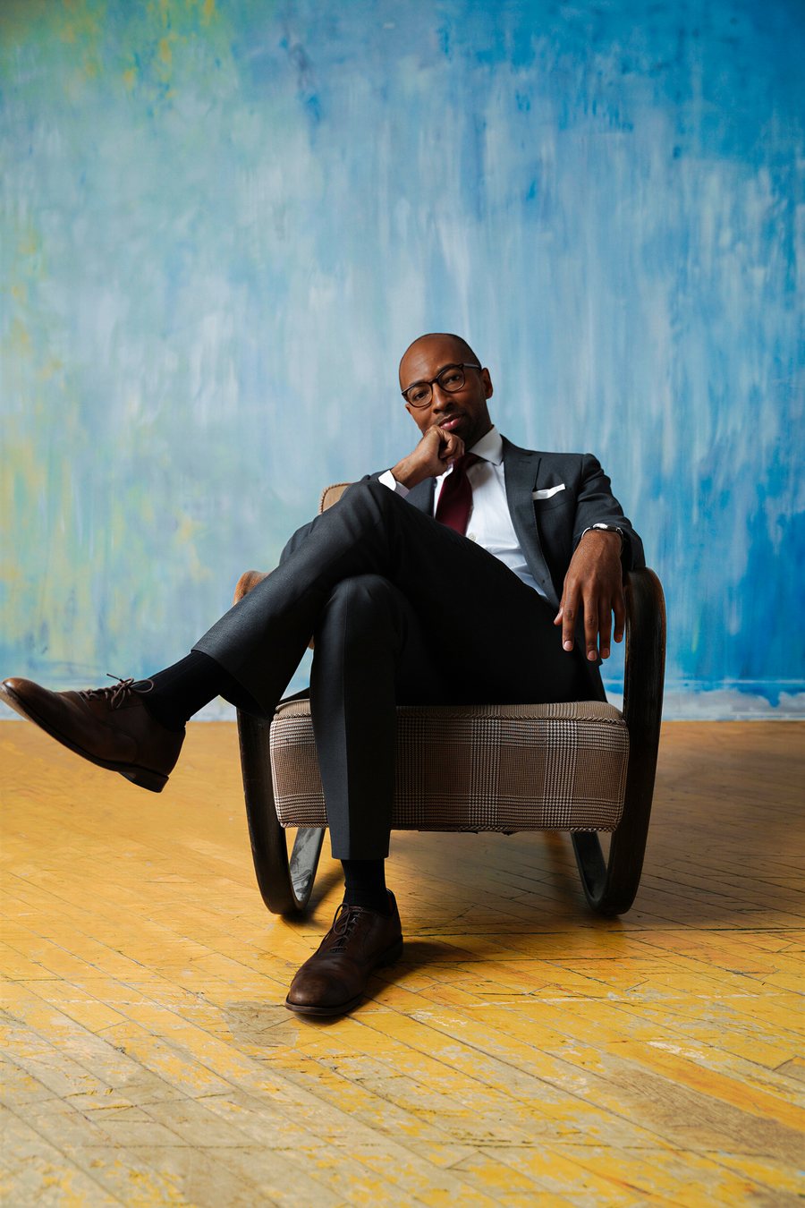 Full length portrait seated in a chair against the blue backdrop